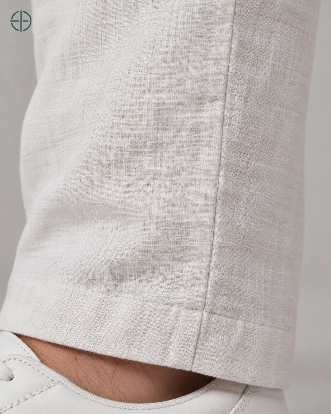 Calça 100% Linho Belga Masculina, cor Branco, Detalhe aproximado do tecido e da costura no modelo, mostrando textura real, em estúdio profissional com fundo cinza ostra.