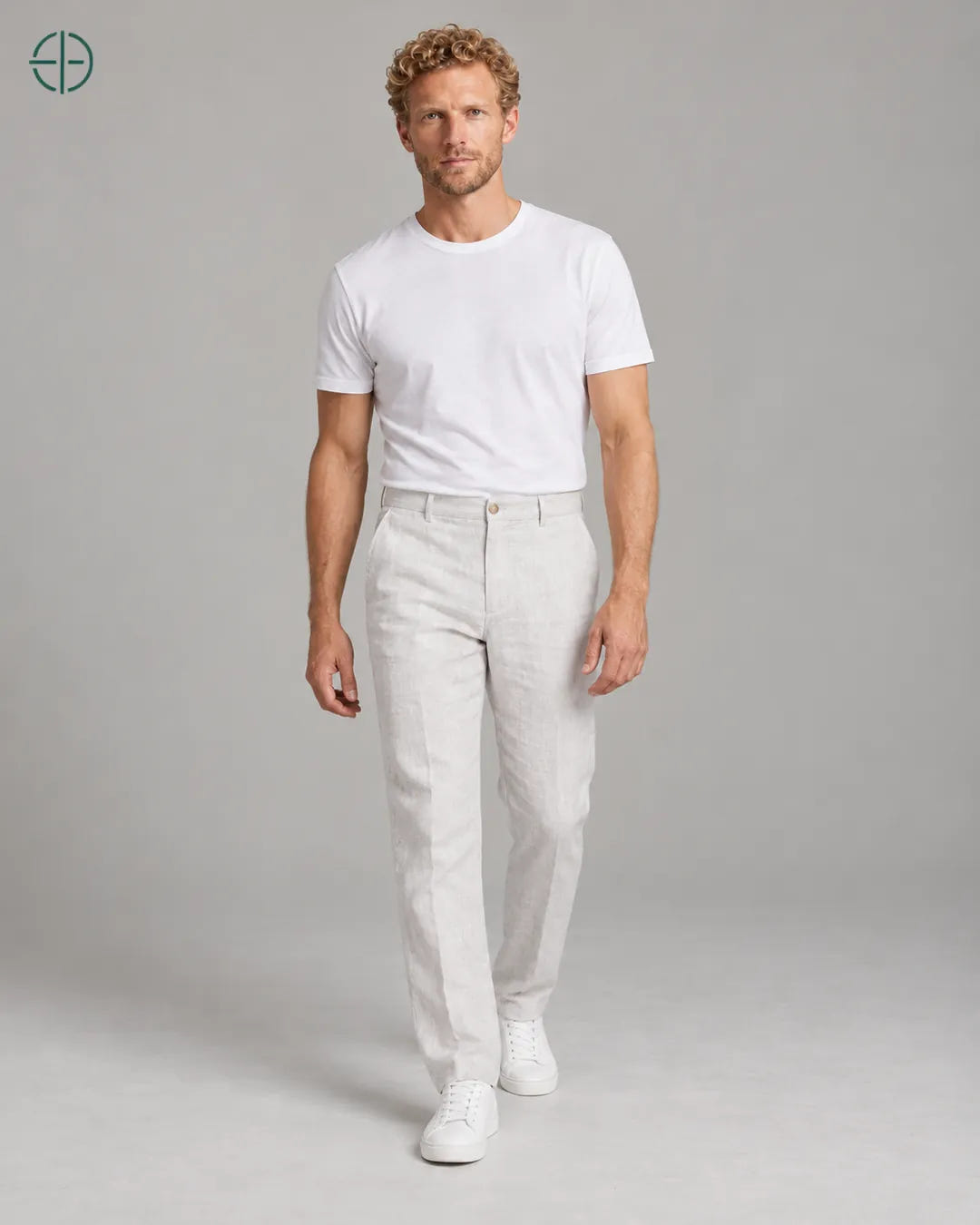 Calça 100% Linho Belga Masculina, cor Branco, Mesmo modelo e roupa em pose natural de três quartos, mostrando o caimento da peça, em estúdio profissional com fundo cinza ostra.