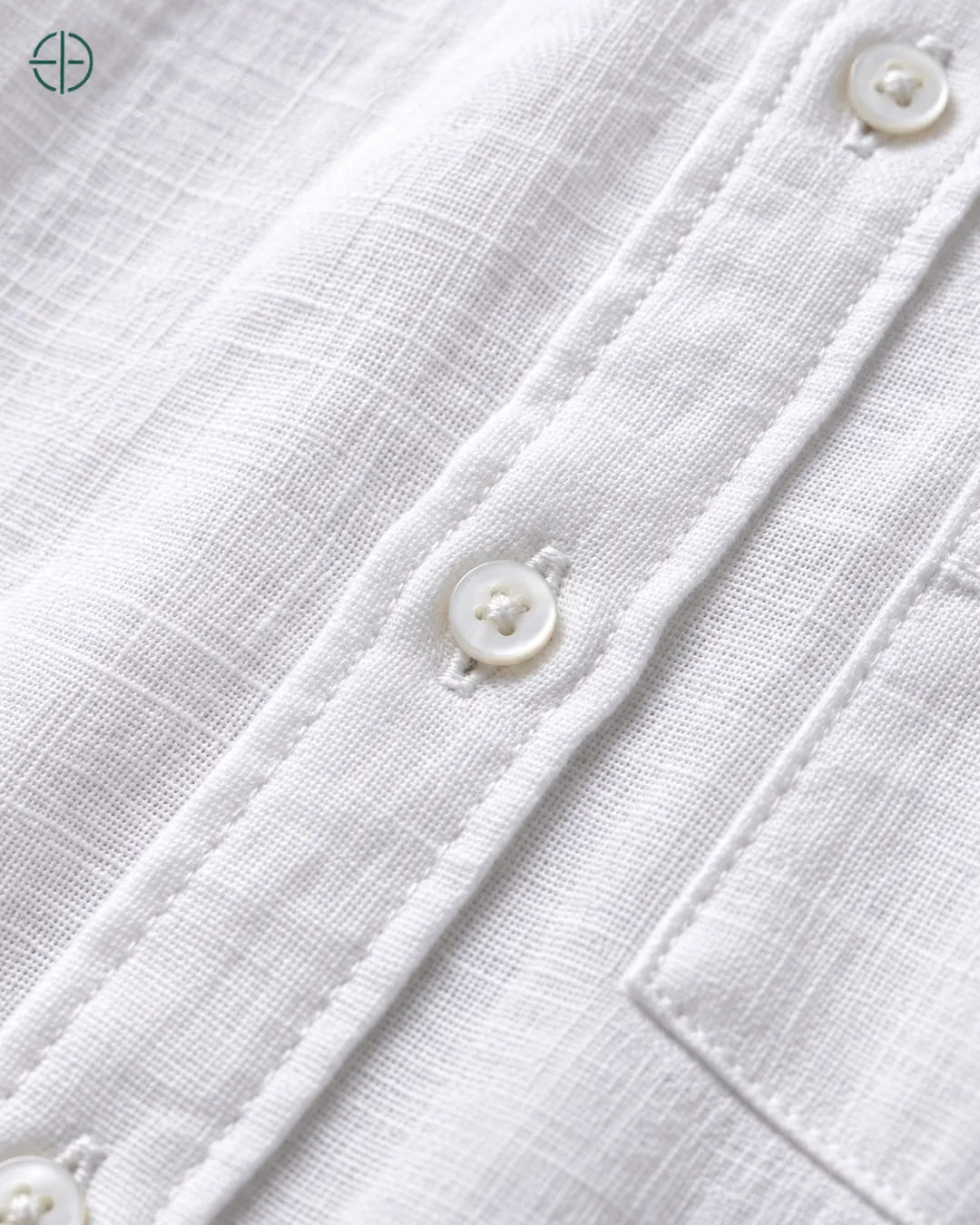 Camisa 100% Linho Belga Masculina, cor Branco, Detalhe aproximado do tecido e da costura no modelo, mostrando textura real, em estúdio profissional com fundo cinza ostra.