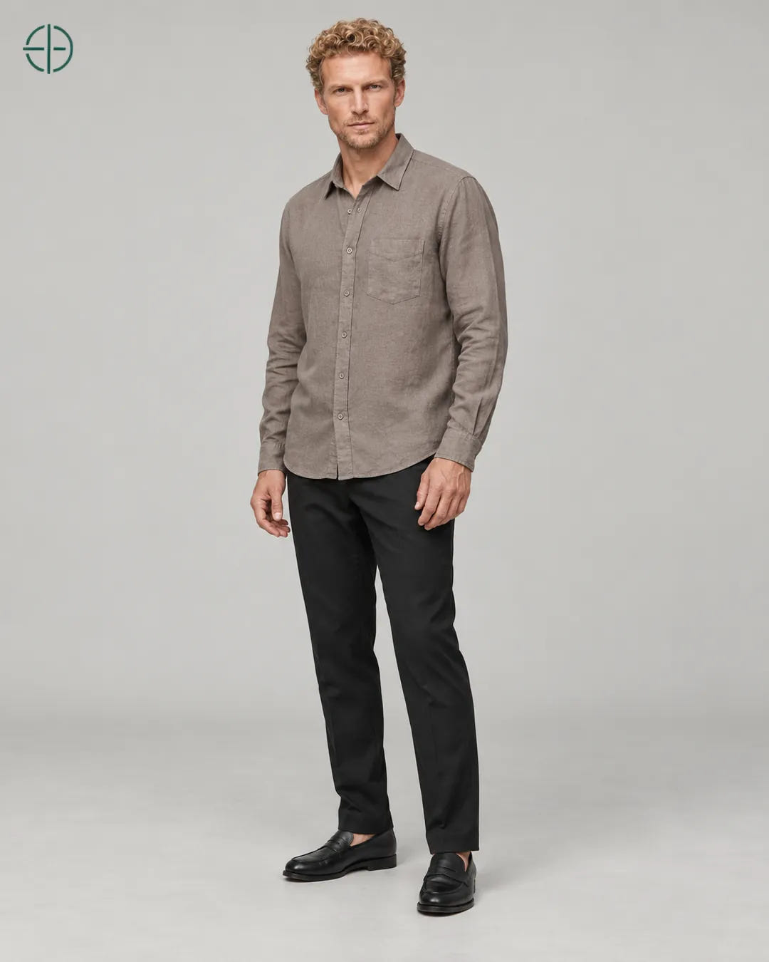 Camisa 100% Linho Belga Masculina, cor Camelo, Mesmo modelo e roupa em pose natural de três quartos, mostrando o caimento da peça, em estúdio profissional com fundo cinza ostra.