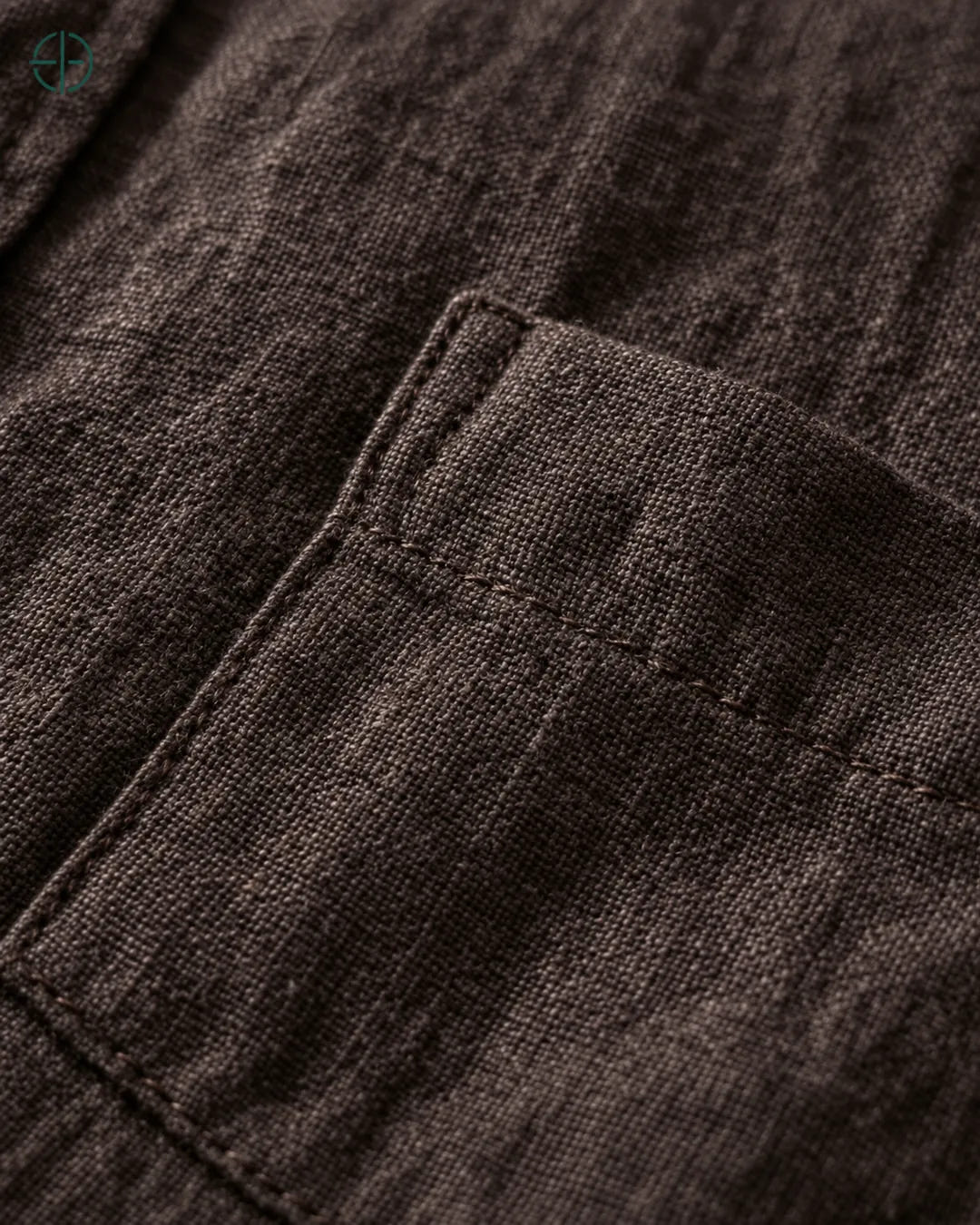 Camisa 100% Linho Belga Masculina, cor Marrom, Detalhe aproximado do tecido e da costura no modelo, mostrando textura real, em estúdio profissional com fundo cinza ostra.