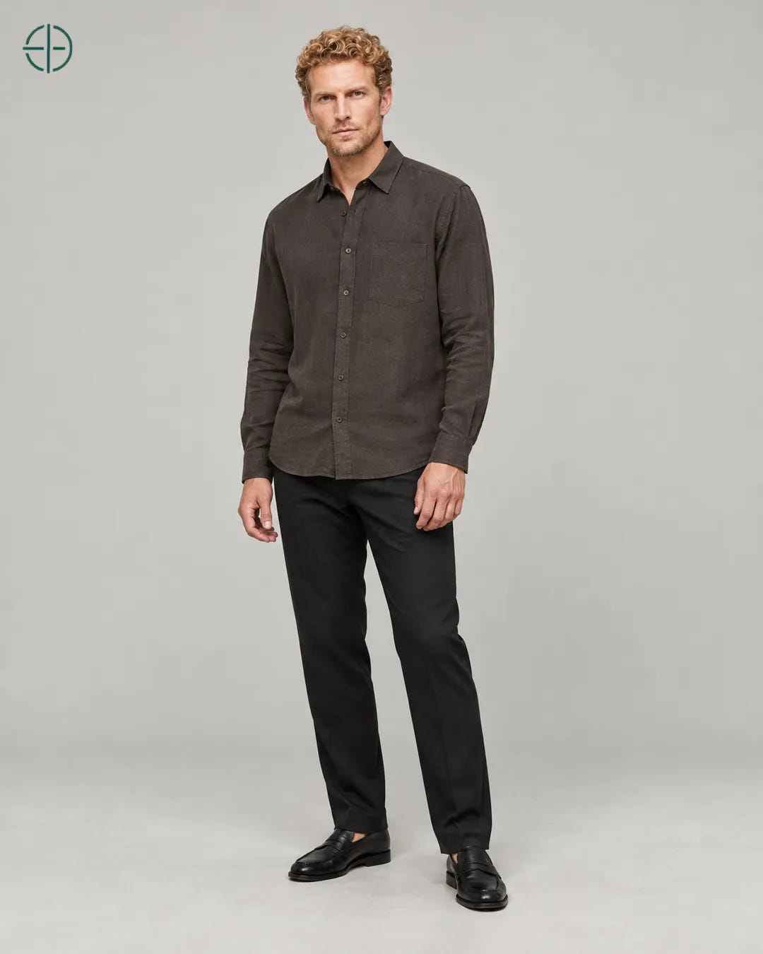 Camisa 100% Linho Belga Masculina, cor Marrom, Mesmo modelo e roupa em pose natural de três quartos, mostrando o caimento da peça, em estúdio profissional com fundo cinza ostra.