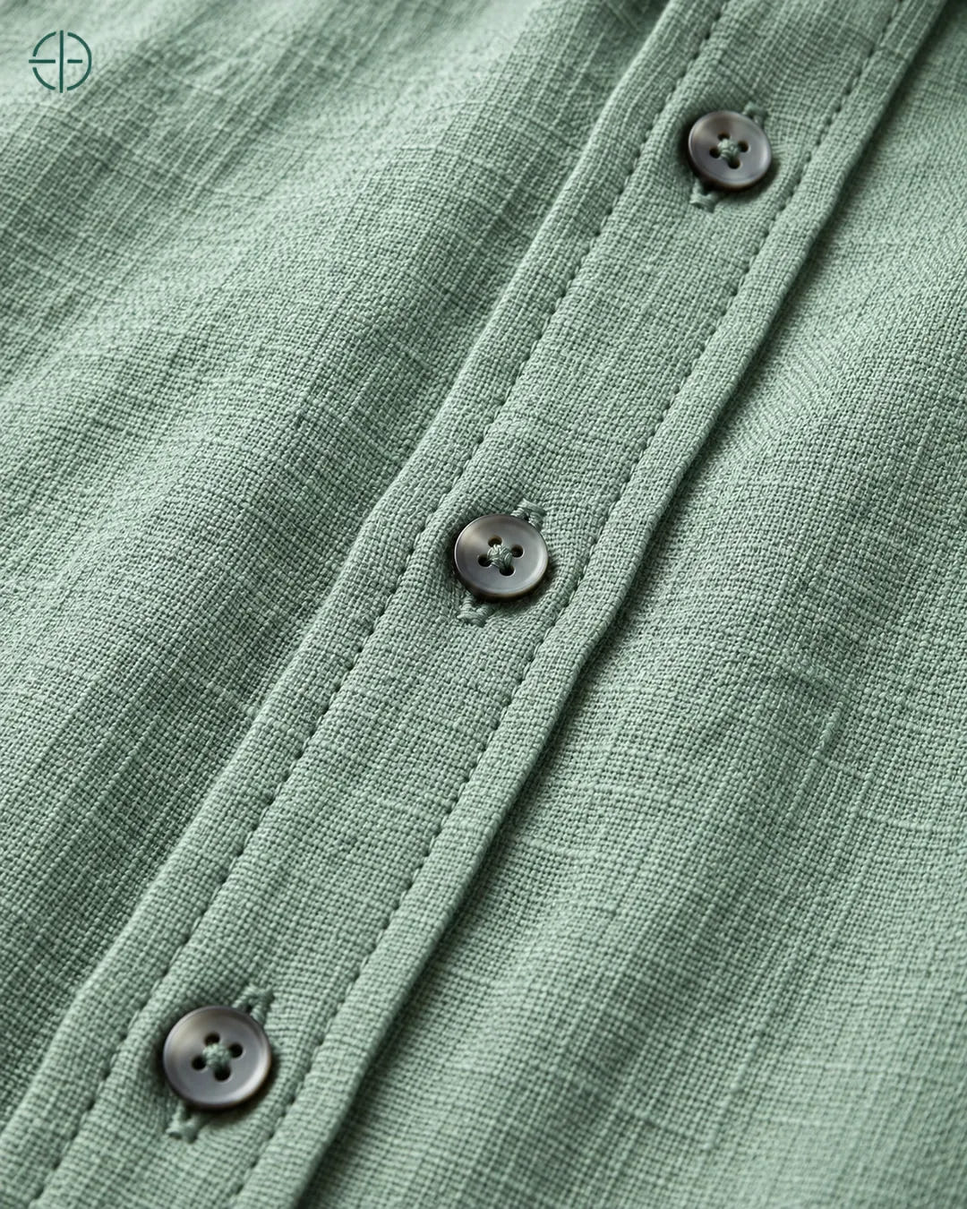 Camisa 100% Linho Belga Masculina Sem Bolso, cor Verde, Detalhe aproximado do tecido e da costura no modelo, mostrando textura real, em estúdio profissional com fundo cinza ostra.