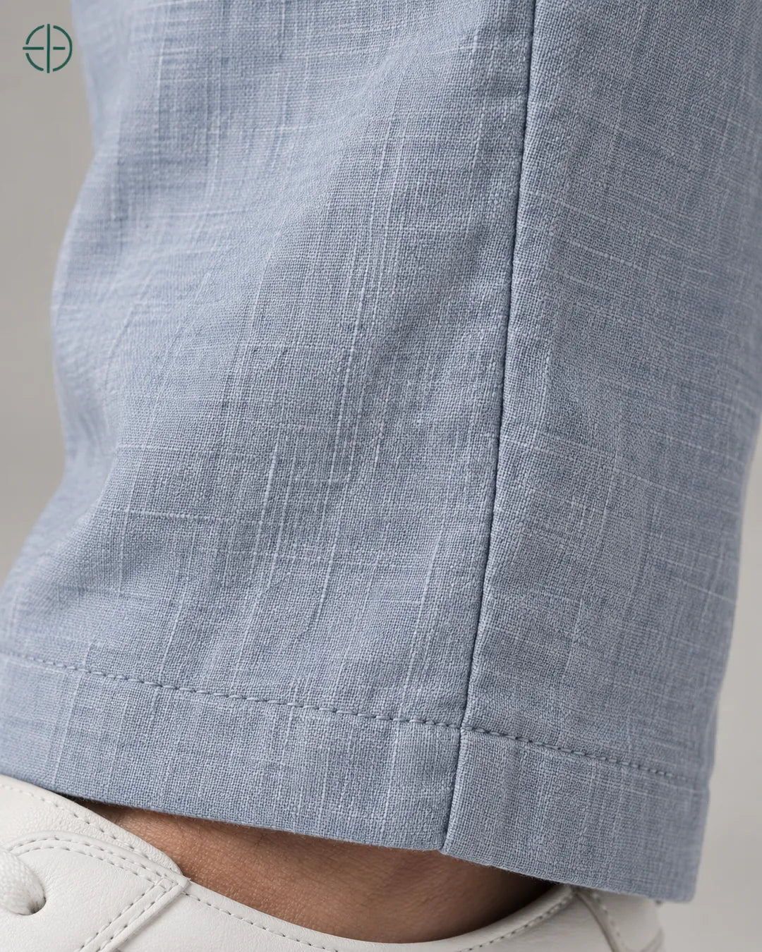 Calça 100% Linho Belga Masculina, cor Azul Claro, Detalhe aproximado do tecido e da costura no modelo, mostrando textura real, em estúdio profissional com fundo cinza ostra.