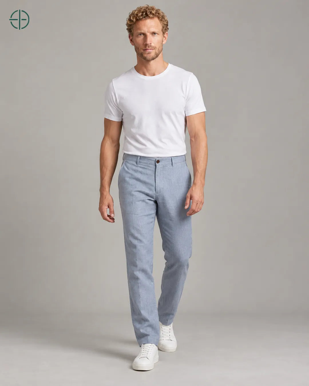 Calça 100% Linho Belga Masculina, cor Azul Claro, Mesmo modelo e roupa em pose natural de três quartos, mostrando o caimento da peça, em estúdio profissional com fundo cinza ostra.