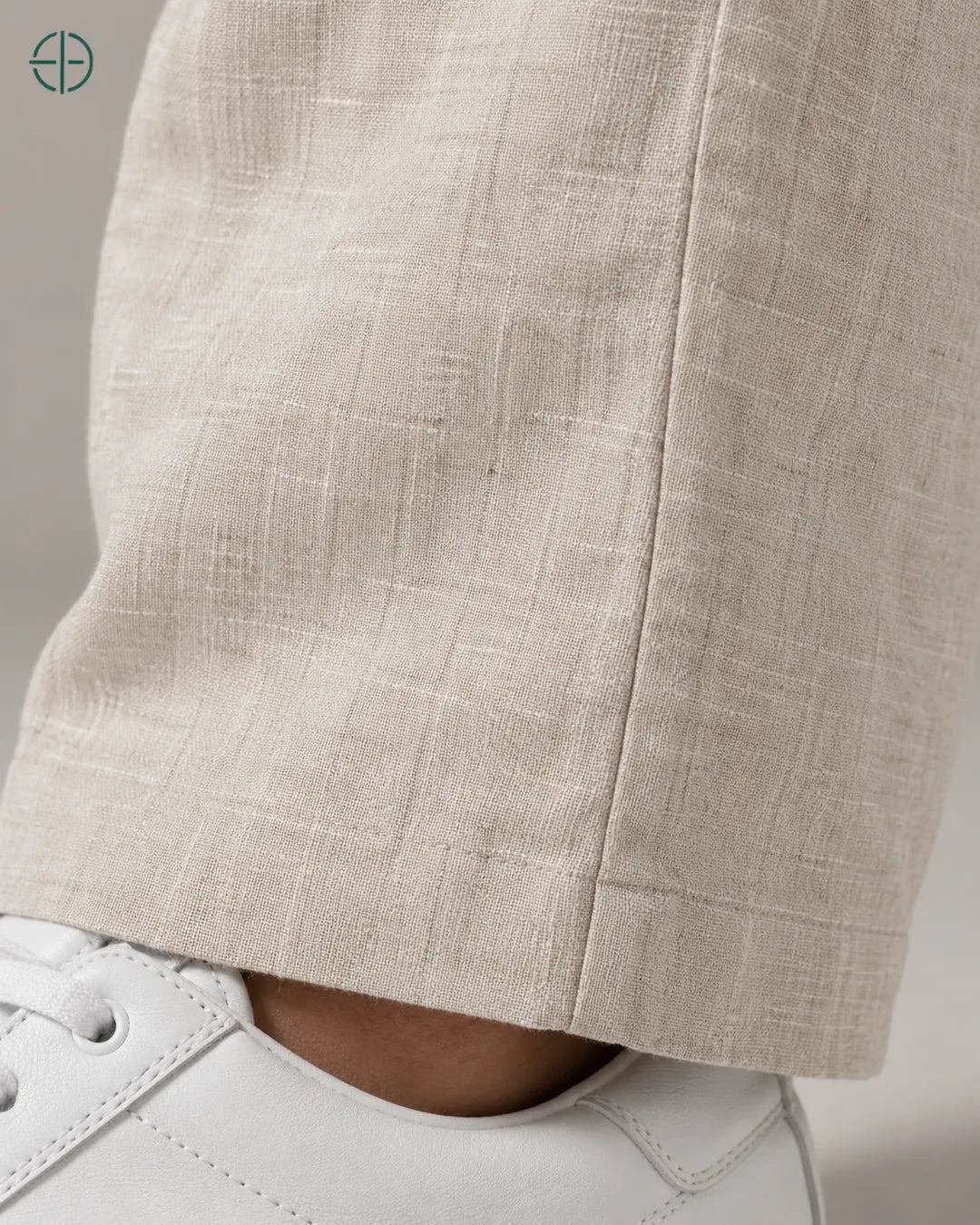Calça 100% Linho Belga Masculina, cor Bege, Detalhe aproximado do tecido e da costura no modelo, mostrando textura real, em estúdio profissional com fundo cinza ostra.