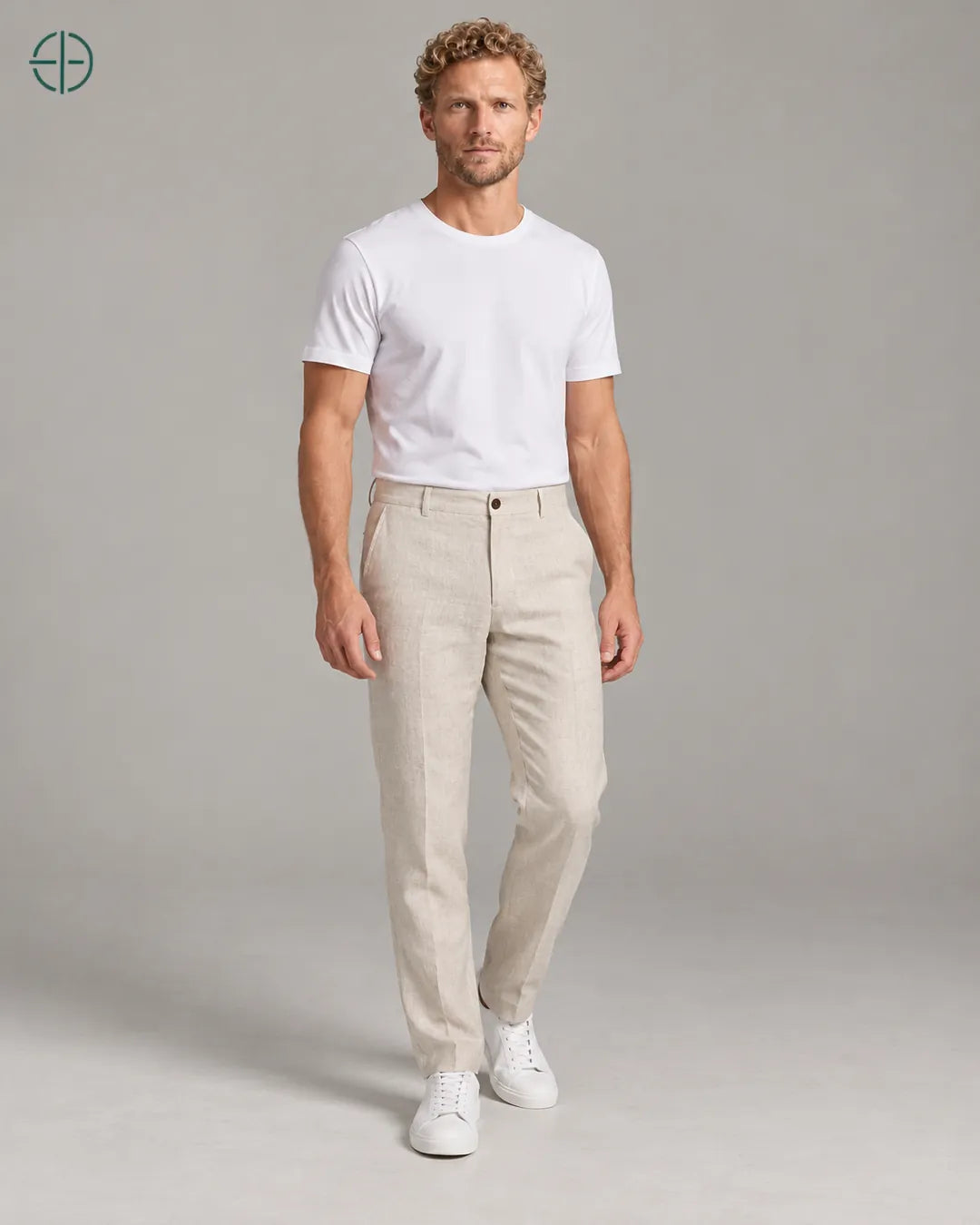 Calça 100% Linho Belga Masculina, cor Bege, Mesmo modelo e roupa em pose natural de três quartos, mostrando o caimento da peça, em estúdio profissional com fundo cinza ostra.