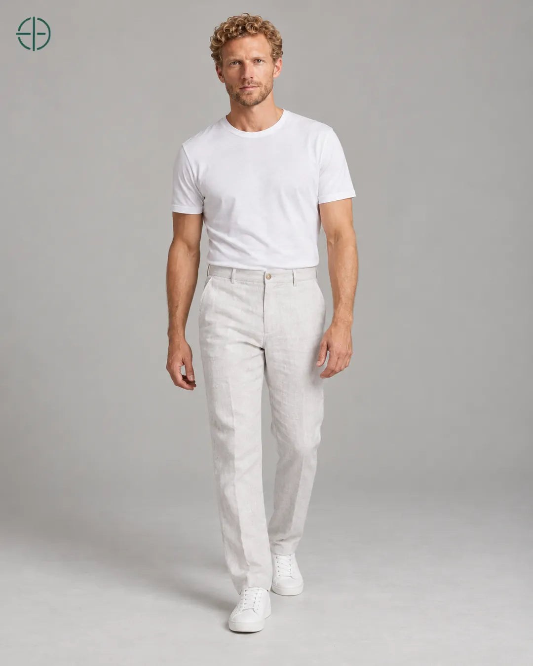 Calça 100% Linho Belga Masculina, cor Branco, Mesmo modelo e roupa em pose natural de três quartos, mostrando o caimento da peça, em estúdio profissional com fundo cinza ostra.