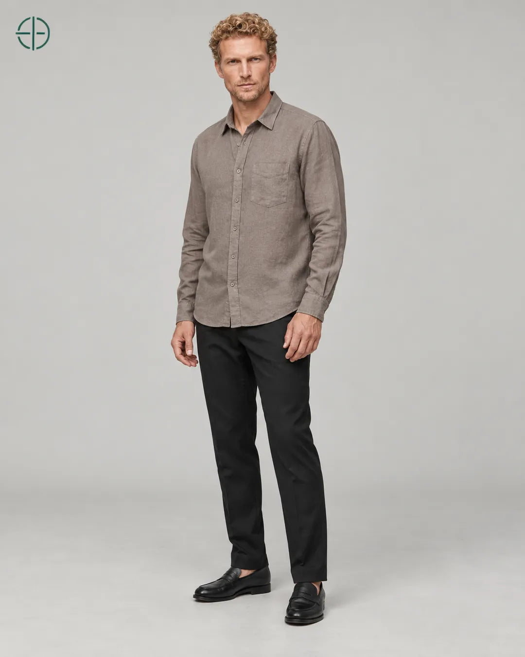 Camisa 100% Linho Belga Masculina, cor Camelo, Mesmo modelo e roupa em pose natural de três quartos, mostrando o caimento da peça, em estúdio profissional com fundo cinza ostra.