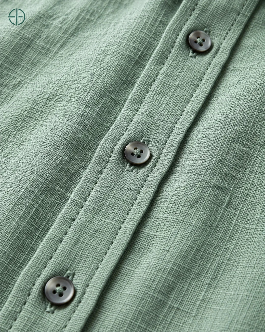 Camisa 100% Linho Belga Masculina Sem Bolso, cor Verde, Detalhe aproximado do tecido e da costura no modelo, mostrando textura real, em estúdio profissional com fundo cinza ostra.